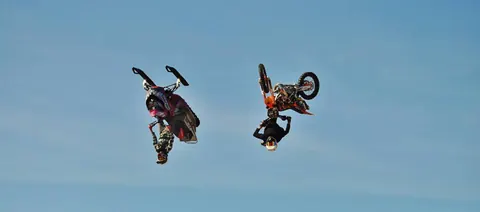 Två FMX-förare voltar sida vid sida mot blå himmel