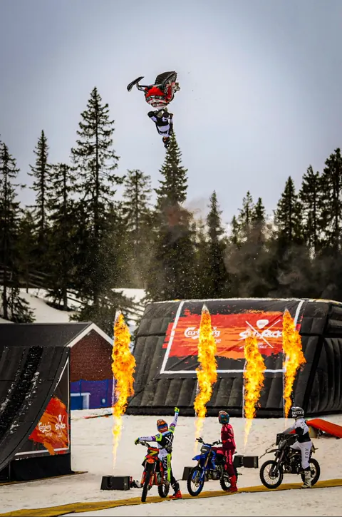 Snöskoter gör backflip ovanför FMX-förarna och eldpelare